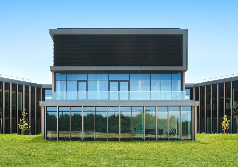 The Nexova Cybersecurity Centre of Excellence: a modern glass and dark-clad building on a green lawn under a blue sky
