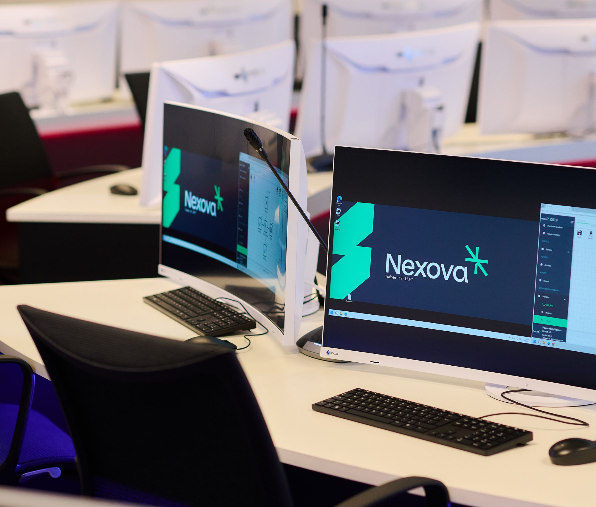 Two curved monitors showing the Nexova logo on desks in a training room at the Cybersecurity Centre of Excellence